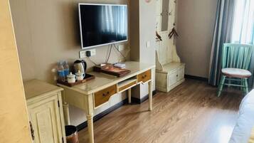 A hotel room with a wooden floor, a desk with a flat-screen TV, a small cabinet, and a chair.