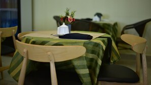 A dining area with a round table covered by a green tablecloth, wooden chairs, and a vase with flowers. - La Stanar Hotel (Dodoma)