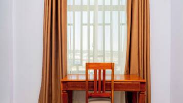 Una mesa de madera con una silla frente a una ventana con cortinas.