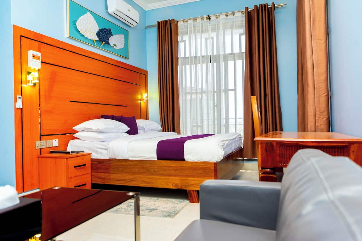 A hotel room with a wooden bed, a desk, a chair, and a window with curtains.