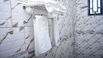 A bathroom with a shower, a towel rack with multiple towels, and a window with a view of the sky.