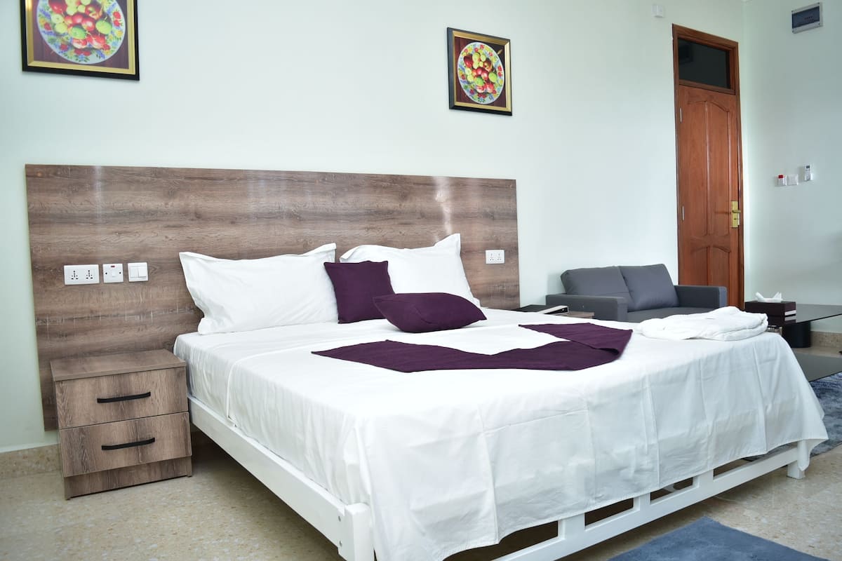 A neatly made bed with white and purple bedding, a wooden headboard, and a small bedside table with drawers.