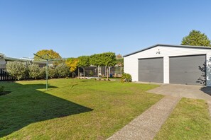 A residential property with a well-maintained lawn, a garage, and a small garden area with trees and shrubs. - The Orchard House - Turangi Holiday Home (Turangi)