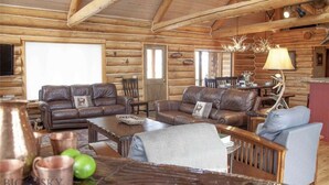 A log cabin interior with leather sofas, a wooden coffee table, and a chandelier. - Yellowstone Inspired Lodge - Two Fireplaces (Dillon)