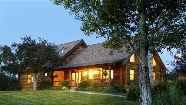 A log cabin with a porch, surrounded by a well-maintained lawn and trees. - Yellowstone Inspired Lodge - Two Fireplaces (Dillon)