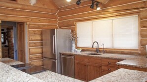 A kitchen with wooden walls, granite countertops, a stainless steel refrigerator, and a window with blinds. - Yellowstone Inspired Lodge - Two Fireplaces (Dillon)