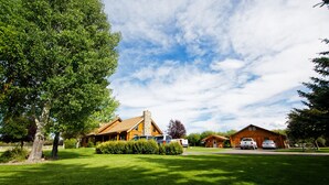 A log cabin with a stone chimney, surrounded by a well-maintained lawn and trees. - Yellowstone Inspired Lodge - Two Fireplaces (Dillon)