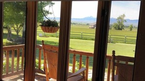 A wooden deck with a hanging planter, a bench, and a view of a green field and mountains. - Yellowstone Inspired Lodge - Two Fireplaces (Dillon)