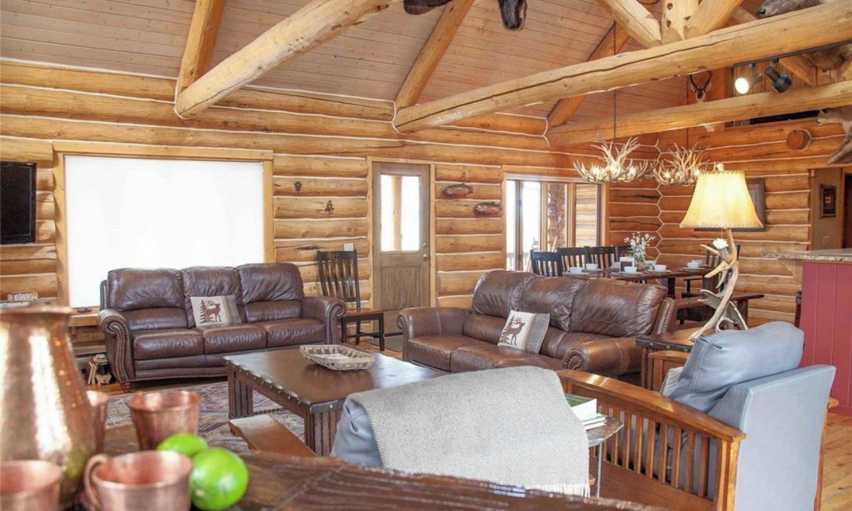 A log cabin interior with leather sofas, a wooden coffee table, and a chandelier.