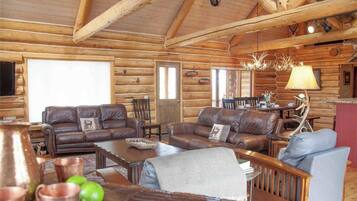 A log cabin interior with leather sofas, a wooden coffee table, and a chandelier.