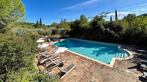 Une piscine rectangulaire, bordée d’une terrasse carrelée et entourée de verdure et d’arbres.