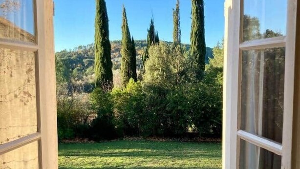 Une fenêtre ouverte donnant sur un jardin, avec de grands arbres et une pelouse.