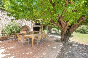 An outdoor patio with a stone-tiled floor, a wooden table with chairs, and a stone wall in the background. - 19th-century country house in Provence (Callas)
