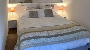 A bedroom with a bed, two bedside lamps, a framed picture on the wall, and a wooden beam above the bed.