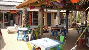 Un espacio al aire libre con mesas y sillas, techo de paja y vista al mar.