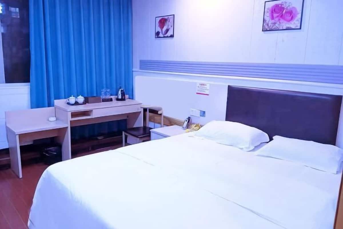 A hotel room with a bed, a desk, a chair, and a window with blue curtains.