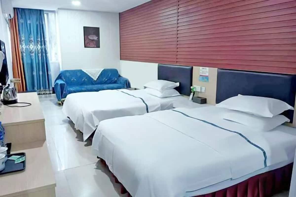 A hotel room with two beds, a blue sofa, a red curtain, and a wall-mounted clock.