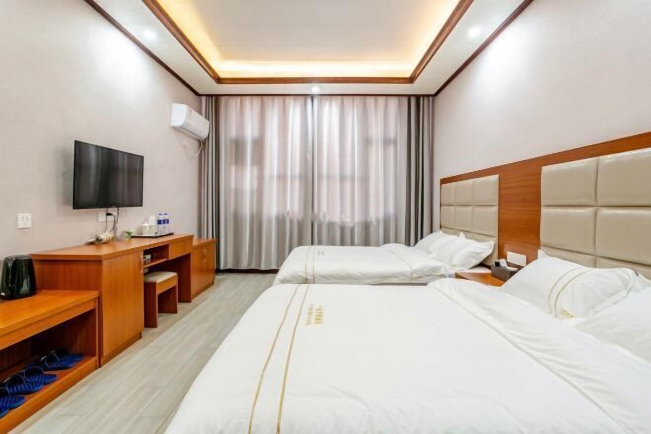 Una habitación de hotel con cama, escritorio, televisor y ventana con cortinas.