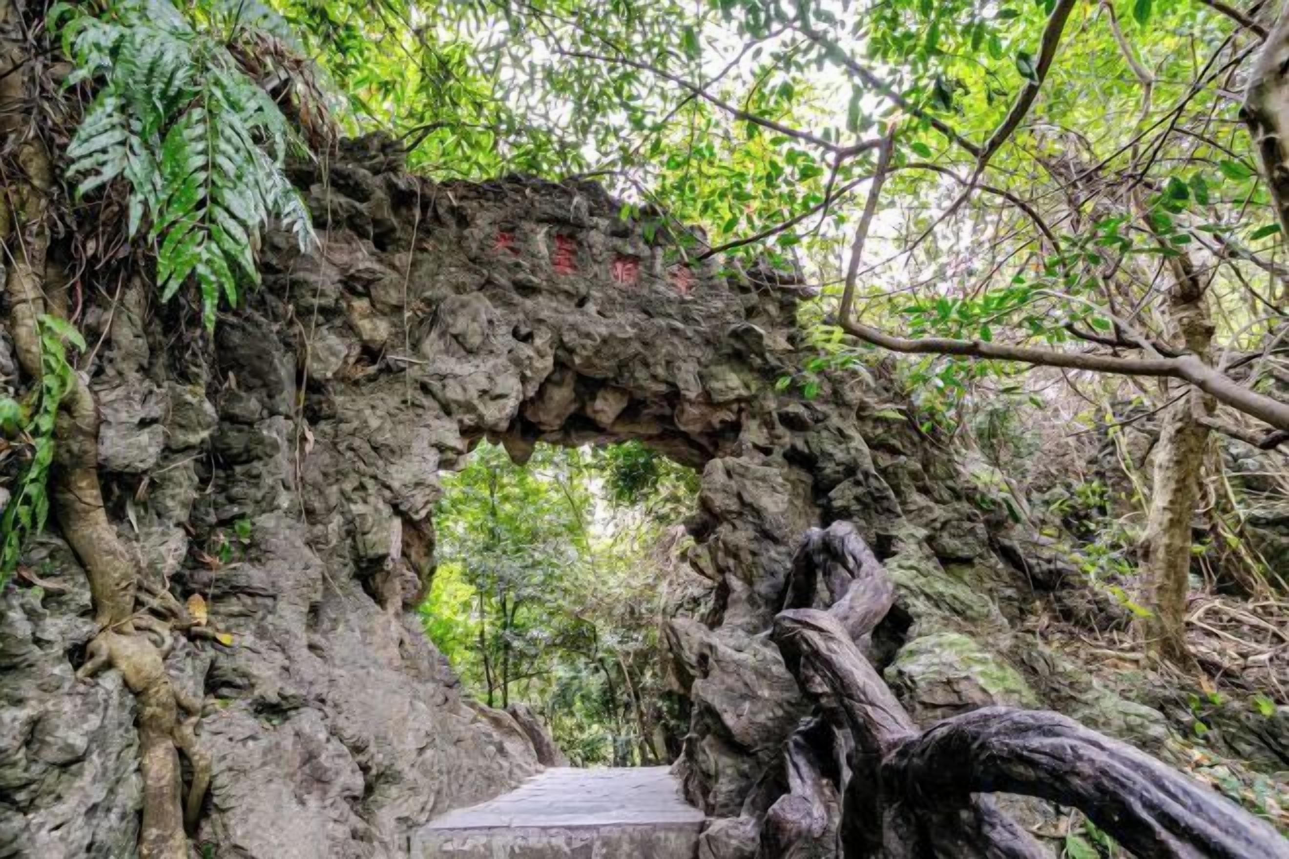 A natural stone archway in a forested area with a wooden platform at the base.