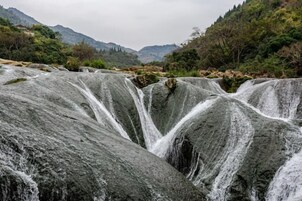 Una cascada se precipita sobre grandes rocas en una zona montañosa.