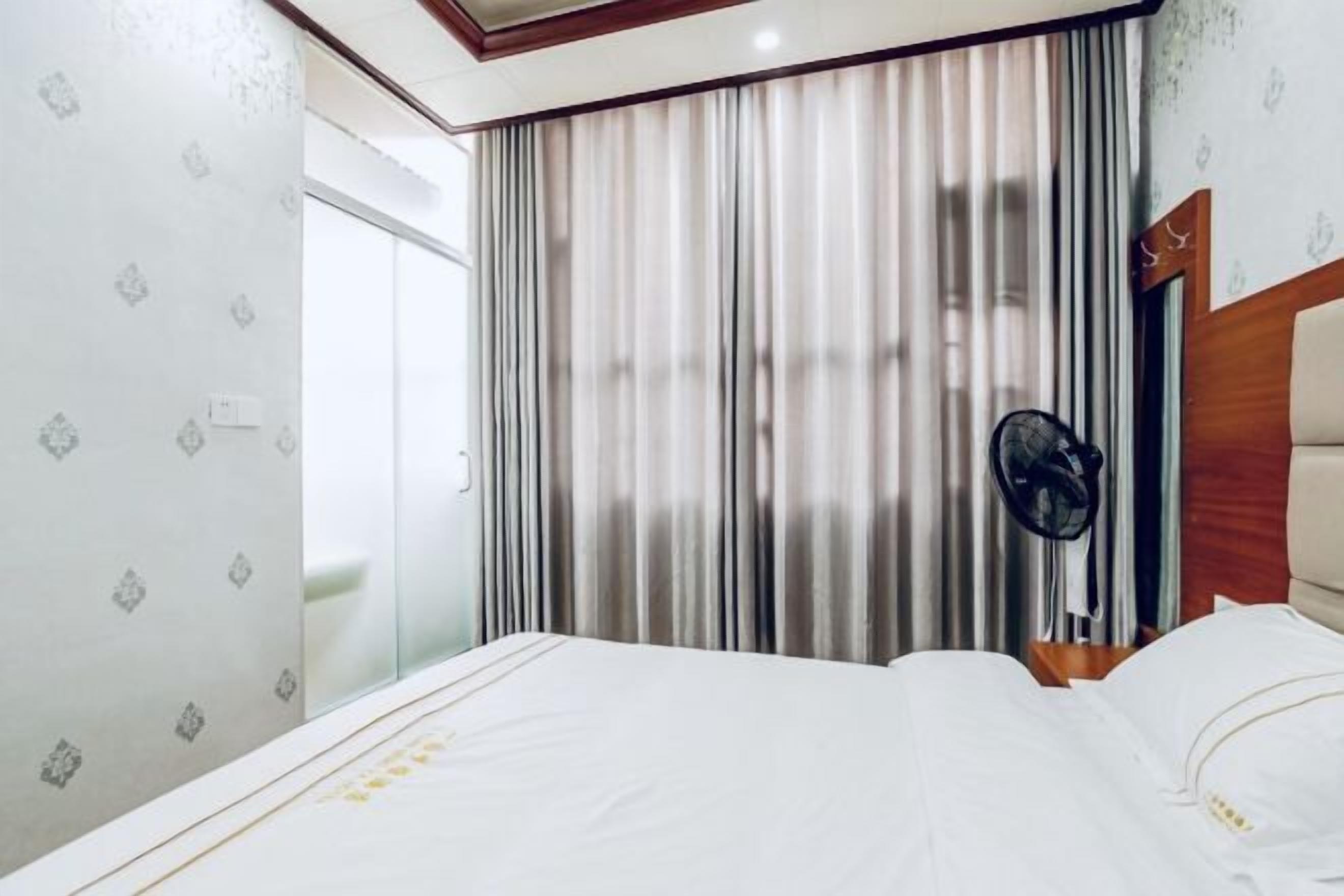 A hotel room with a bed, curtains, a fan, and a wooden headboard.