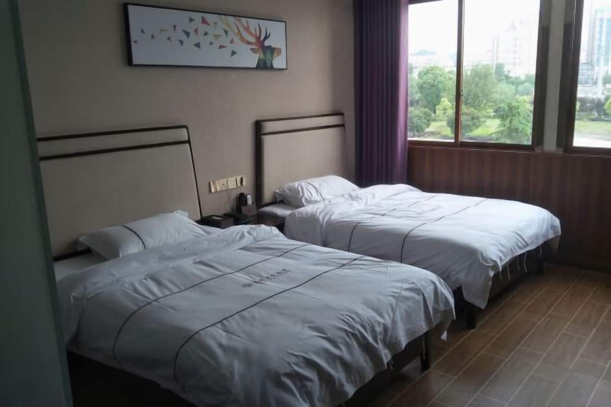 Habitación de hotel con dos camas, una mesita de noche, una lámpara de pared y una ventana con vistas a zonas verdes.