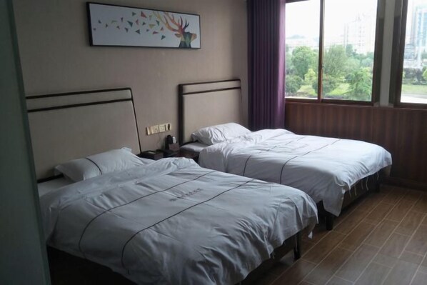 A hotel room with two beds, a nightstand, a wall-mounted light, and a window with a view of greenery. - Luanchuan Friendship Business Hotel (Suichuan)