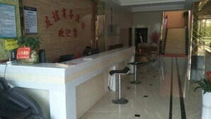 Un espace d’accueil d’hôtel comprenant un comptoir de réception, plusieurs tabourets de bar, une plante en pot et un escalier menant à l’étage supérieur.