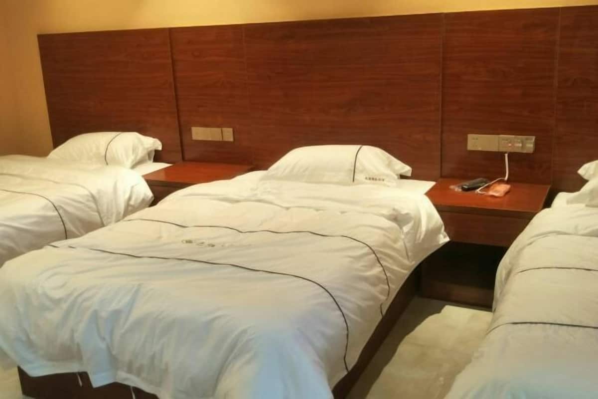 Habitación de hotel con dos camas individuales, cabecero de madera, mesitas de noche y un panel de control en la pared.