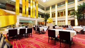A spacious indoor dining area with multiple tables and chairs, high ceilings, and a central decorative sculpture.