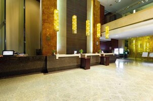 Un área de recepción con piso de mármol, un mostrador de recepción y luminarias verticales.