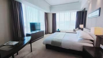 Quarto de hotel com cama, escrivaninha, televisão e janela com cortinas.