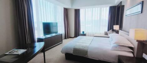 A hotel room with a bed, a desk, a television, and a window with curtains.