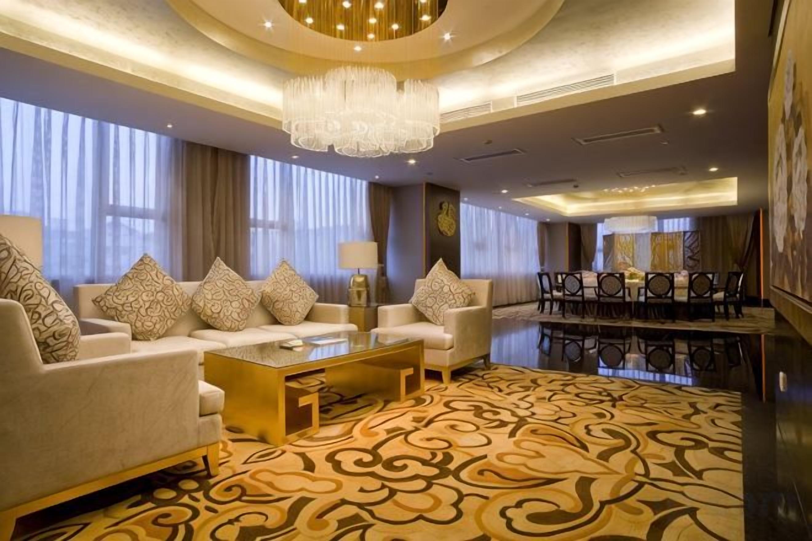 A hotel lobby with a sofa set, a coffee table, a chandelier, and a dining area.
