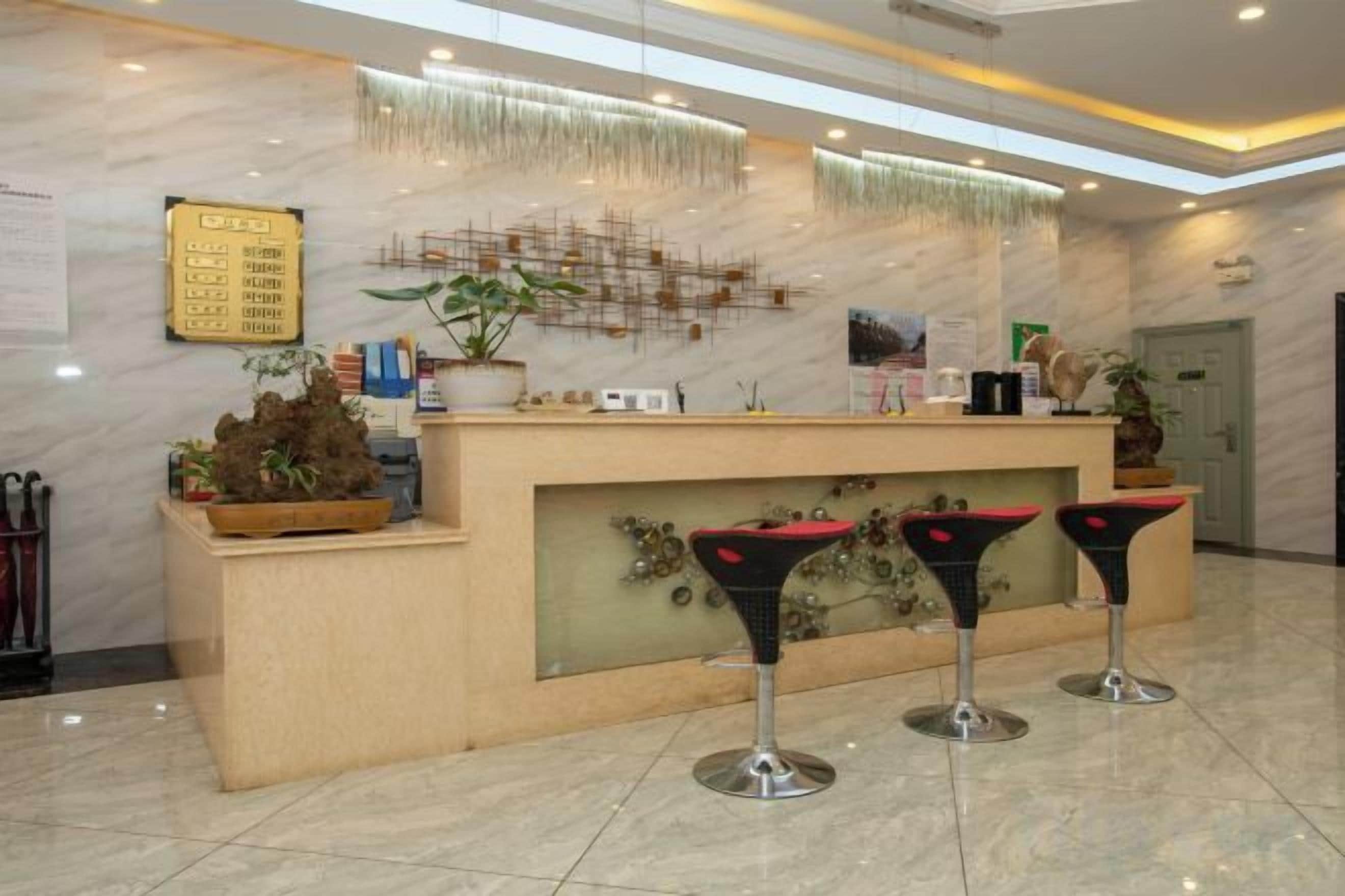 A reception area with a marble counter, two bar stools, a plant, and a wall-mounted menu board.