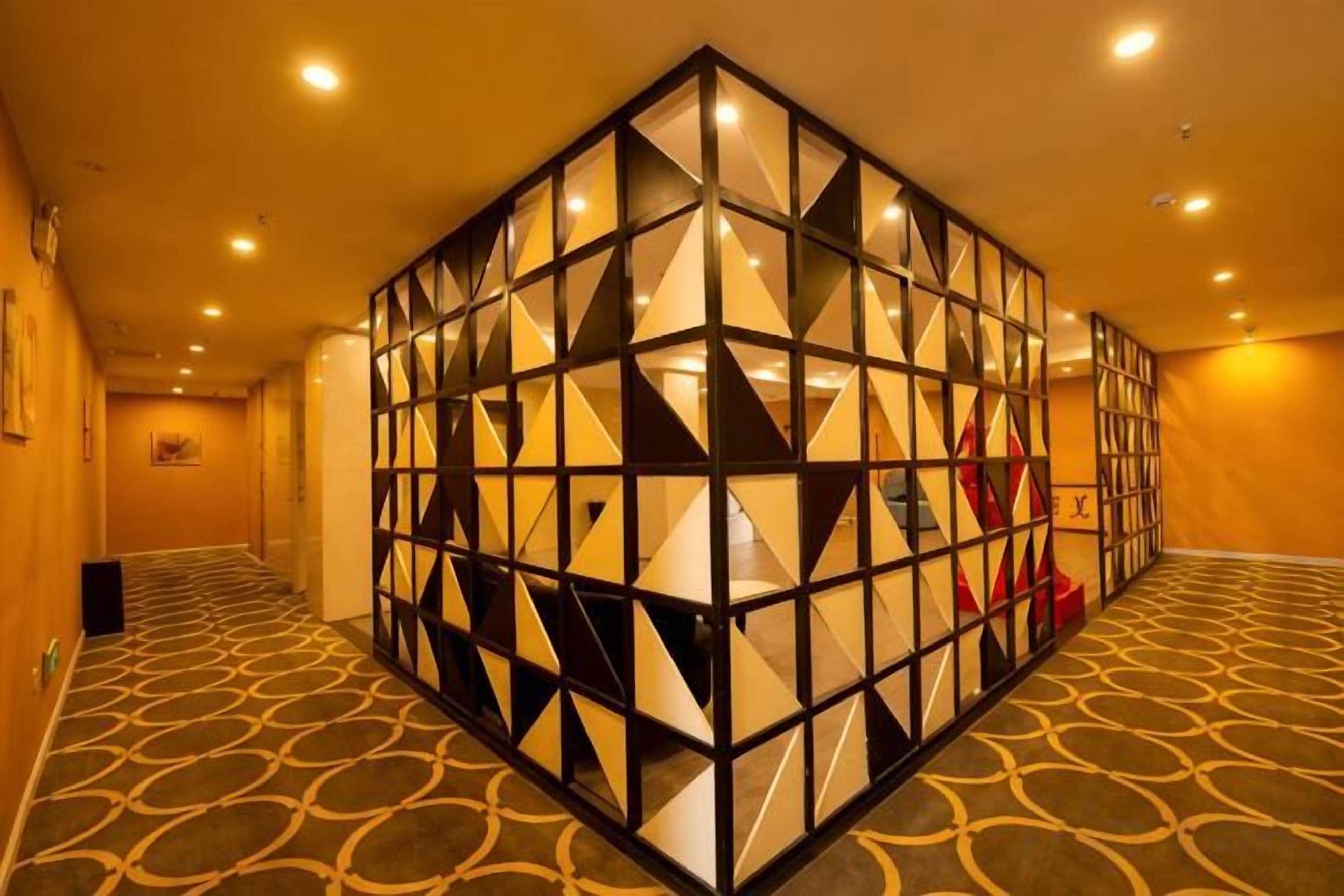 Un pasillo de hotel con una estructura de pared geométrica, alfombra estampada e iluminación empotrada.