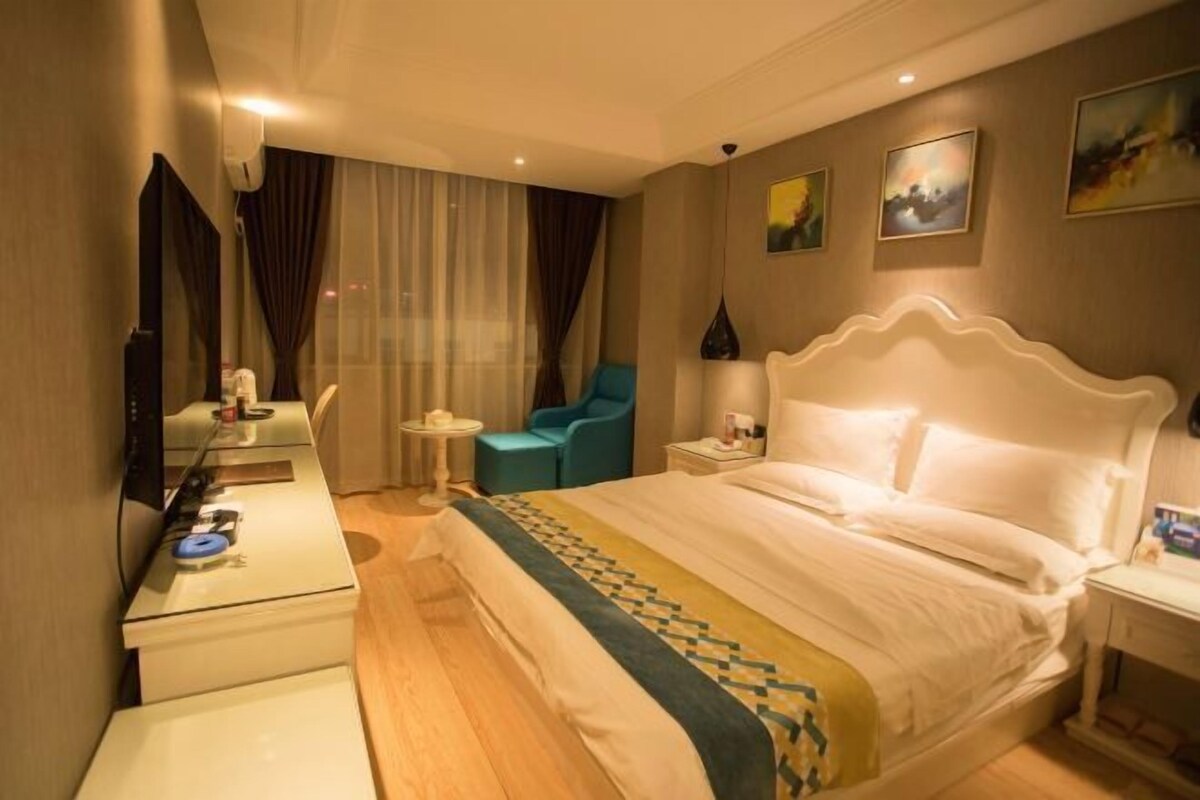 A hotel room with a large bed, a desk, a chair, and a small table.