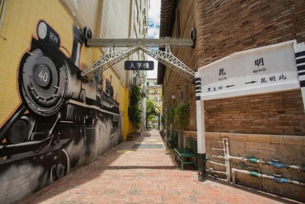 Un estrecho callejón con un mural de un tren a la izquierda y un cartel con caracteres chinos a la derecha.
