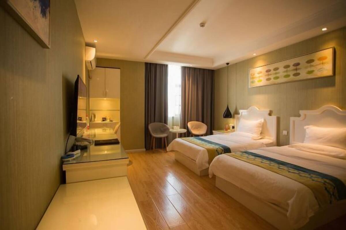 Une chambre d’hôtel avec deux lits, un bureau, une chaise, un miroir et une fenêtre avec des rideaux.