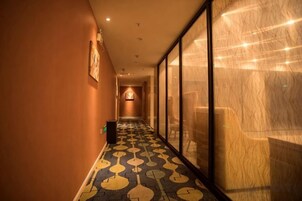 Pasillo de hotel con suelo estampado, un bote de basura y una pared de vidrio en un lateral.