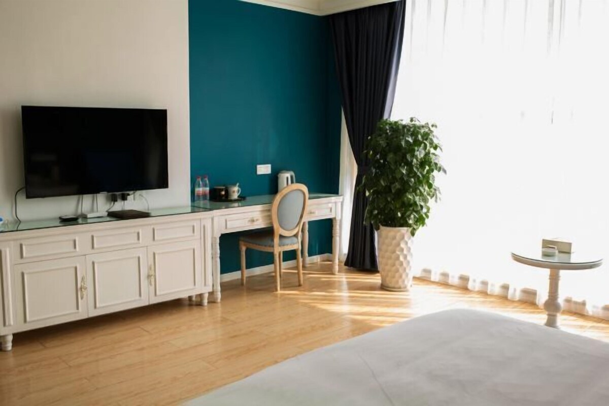 Habitación de hotel con cama, escritorio con silla, televisor, planta en maceta y una mesita.