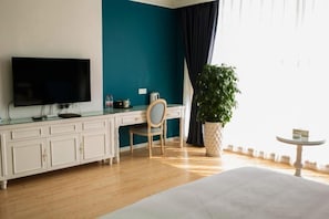 Habitación de hotel con cama, escritorio con silla, televisor, planta en maceta y una mesita.