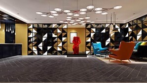 Eine moderne Lobby mit geometrischem Wanddesign, einer zentralen roten Skulptur und zeitgenössischer Sitzmöbel.