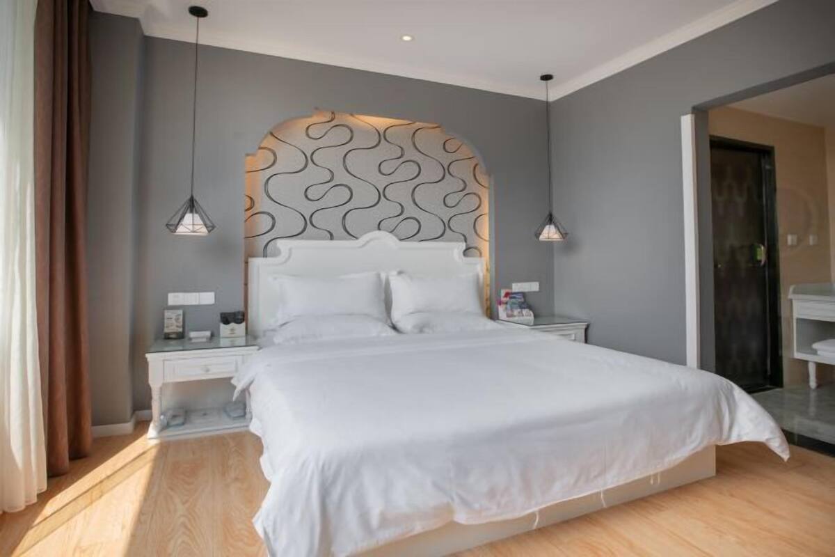 Une chambre à coucher moderne avec un grand lit, une tête de lit décorative, des tables de chevet et des lampes suspendues.