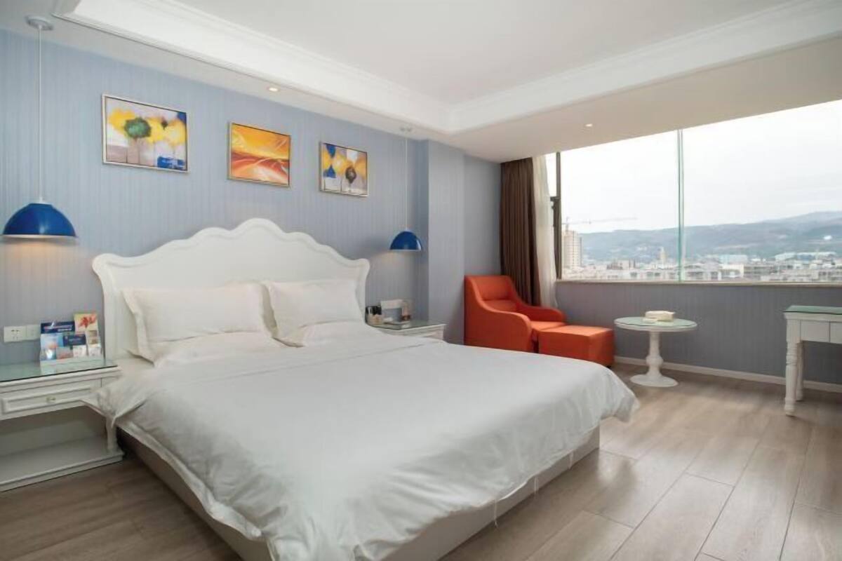 Une chambre d’hôtel avec un grand lit, deux tables de chevet, une chaise, une petite table et des œuvres d’art accrochées au mur.