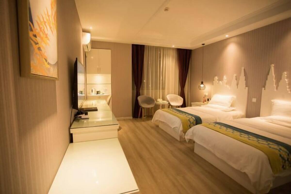 Une chambre d’hôtel avec deux lits, un bureau, une chaise, un miroir et une décoration murale représentant un paysage urbain.