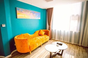 A room with a sofa, a small round table, and a painting on the wall. - Kangjie Hotel (Kaiyuan)