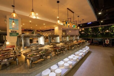 A buffet setup with multiple food stations and a long counter with plates.. Kangjie Hotel