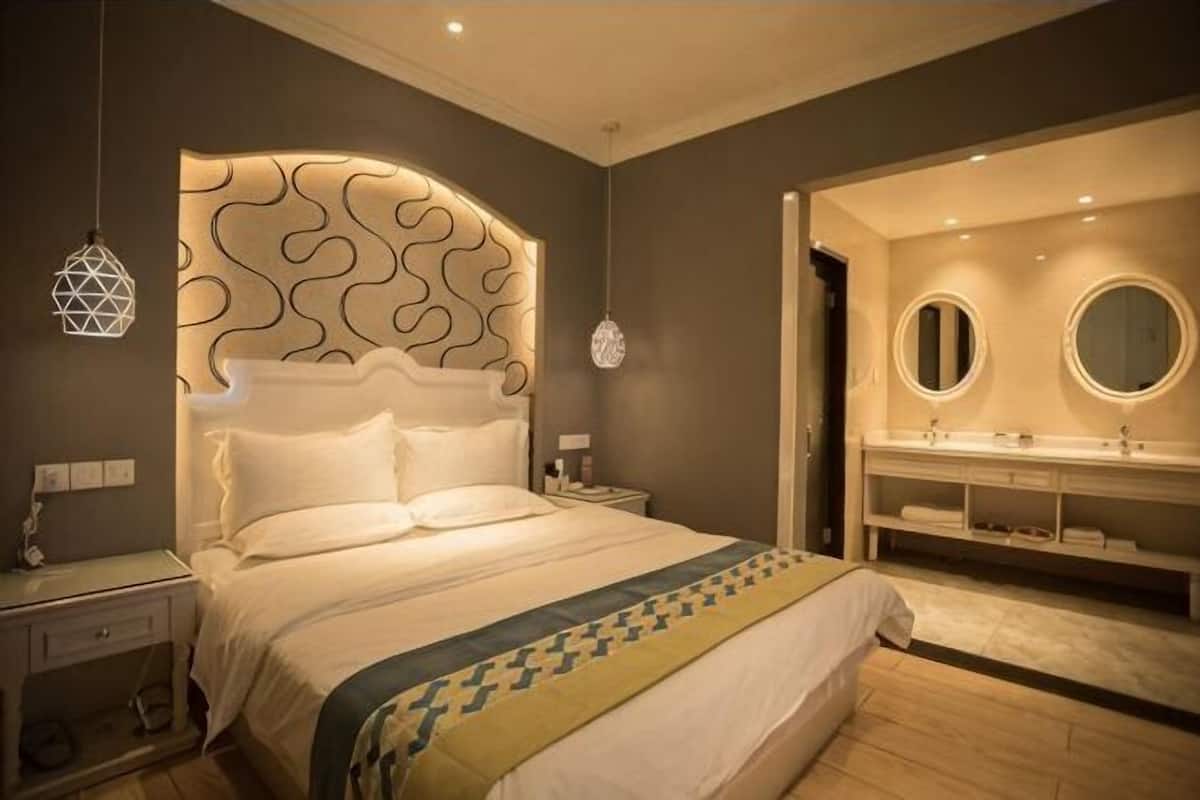 Une chambre d’hôtel moderne avec un grand lit, une table de chevet, une commode et une salle de bain équipée d’un meuble-lavabo et d’un miroir.