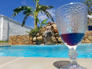 Een glas rode wijn voor een zwembad met een waterval en palmbomen.